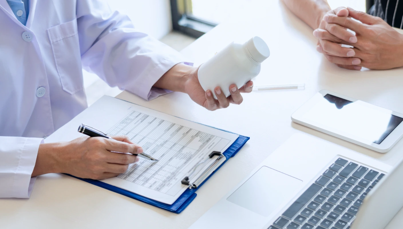 노트북이 있는 테이블에 앉아 고객과 상담 중인 약사의 상체